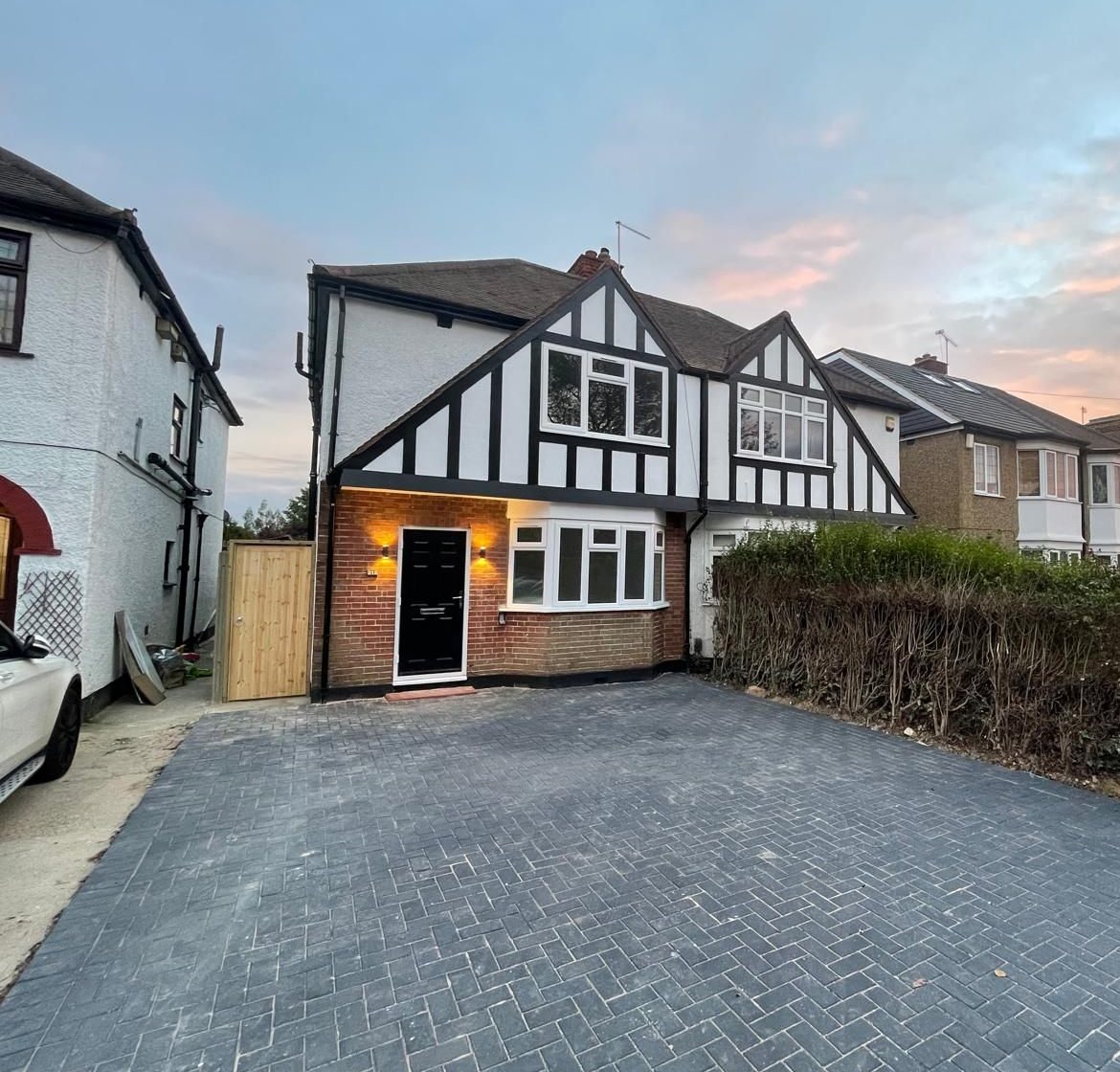 The finished house at dusk, with a new first floor in black timber cladding and a new block-paved driveway