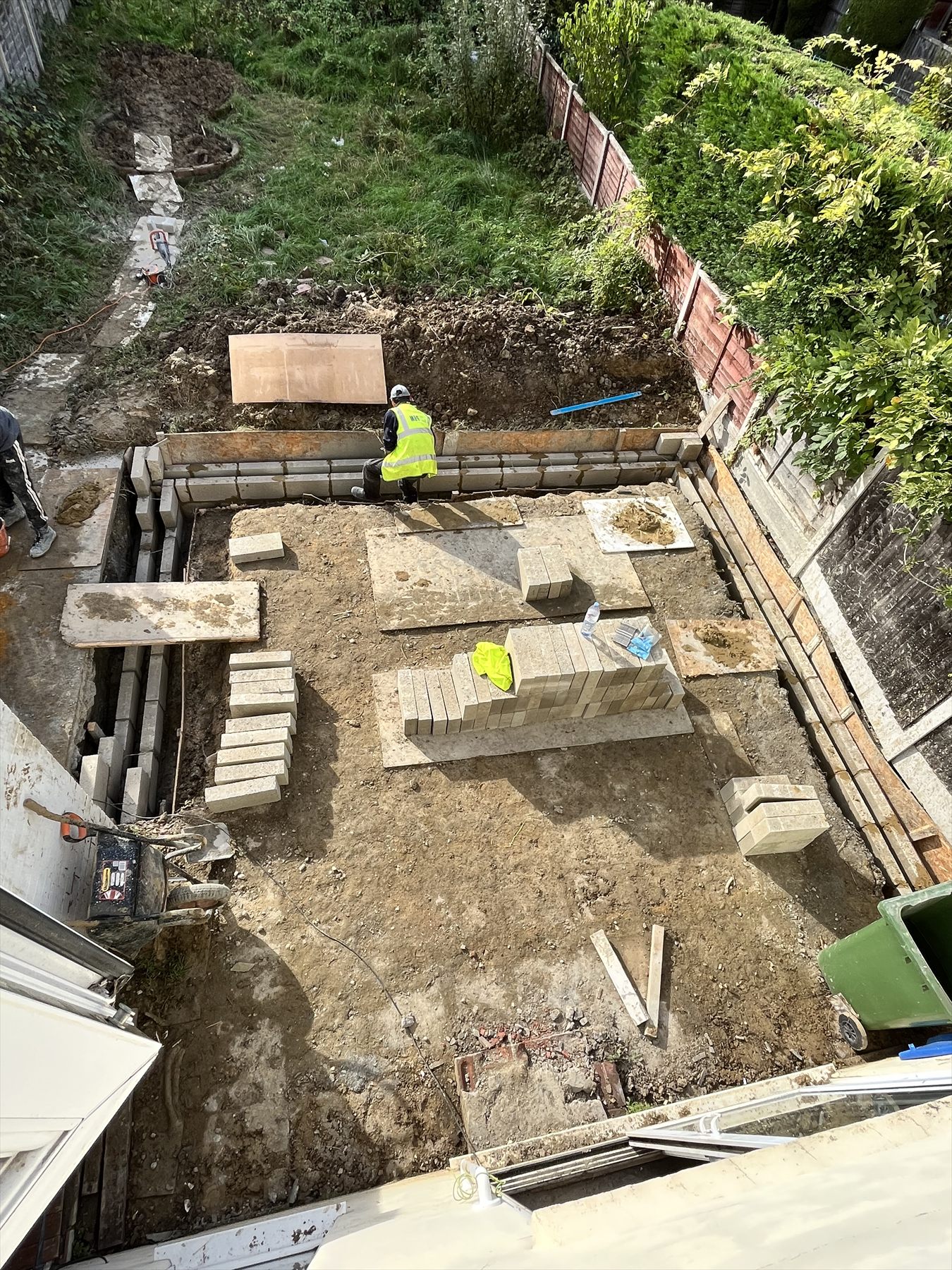Groundworker laying a new patio in a rear garden, with stacks of paving slabs ready to lay