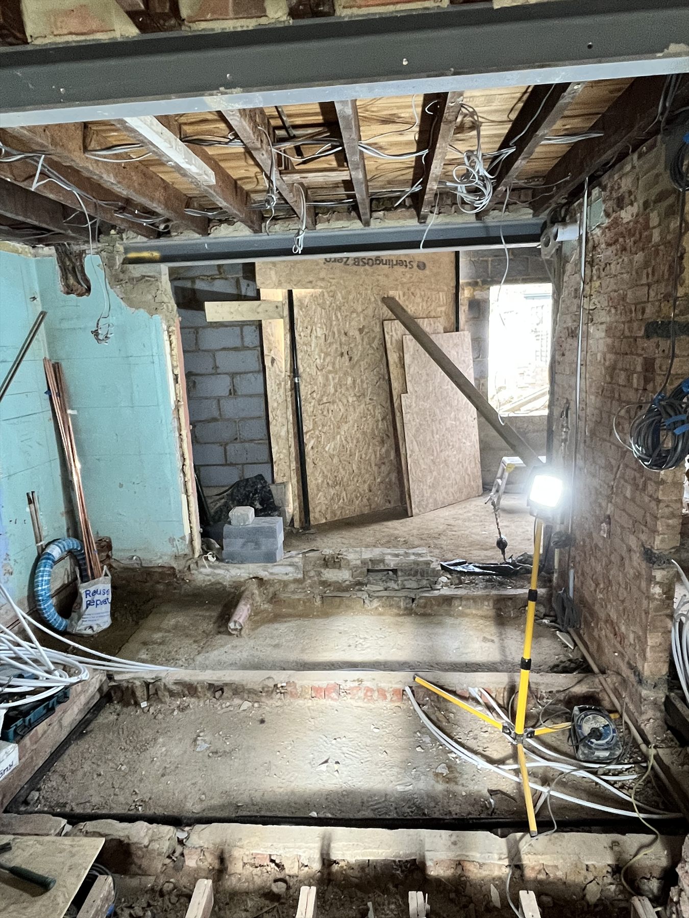 A stripped-out room mid-renovation, with floor and ceiling joists, wiring and blockwork exposed